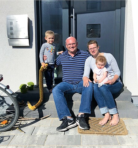 Vierköpfige Familie Riedel sitzt am Eingang ihres Hauses